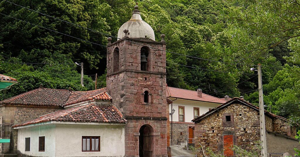 Iglesia y casas de piedra del pueblo de La Riera, en Somiedo (Asturias), donde se ubica la central hidroeléctrica, con la ladera arbolada al fondo