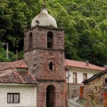 Iglesia y casas de piedra del pueblo de La Riera, en Somiedo (Asturias), donde se ubica la central hidroeléctrica, con la ladera arbolada al fondo
