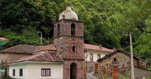Iglesia y casas de piedra del pueblo de La Riera, en Somiedo (Asturias), donde se ubica la central hidroeléctrica, con la ladera arbolada al fondo